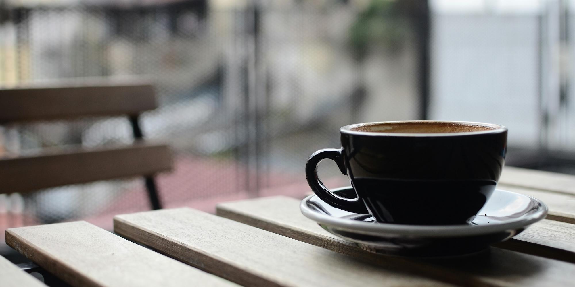 Cover image for this post: A black coffee mug and saucer on a brown wooden table during daytime.