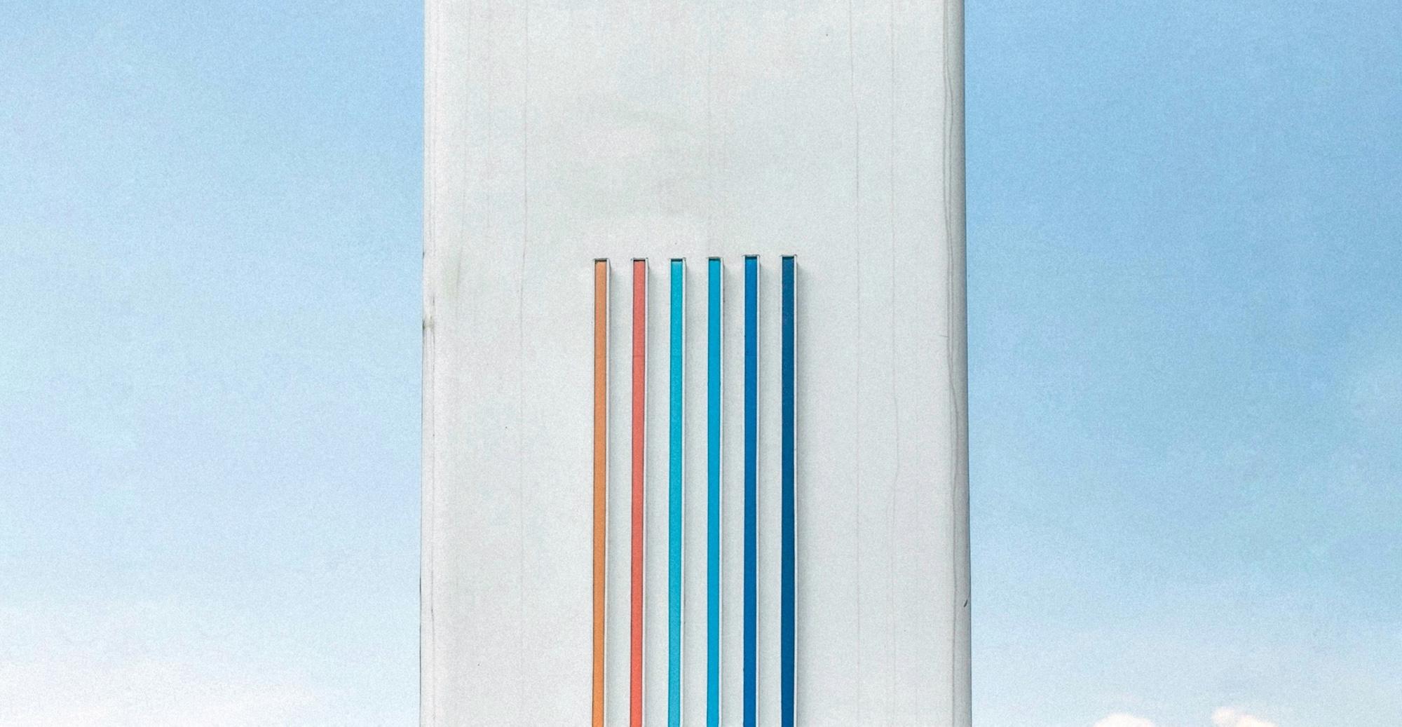 Cover image for this post: A tall white building with vertical colored lines, with a blue sky in the background.