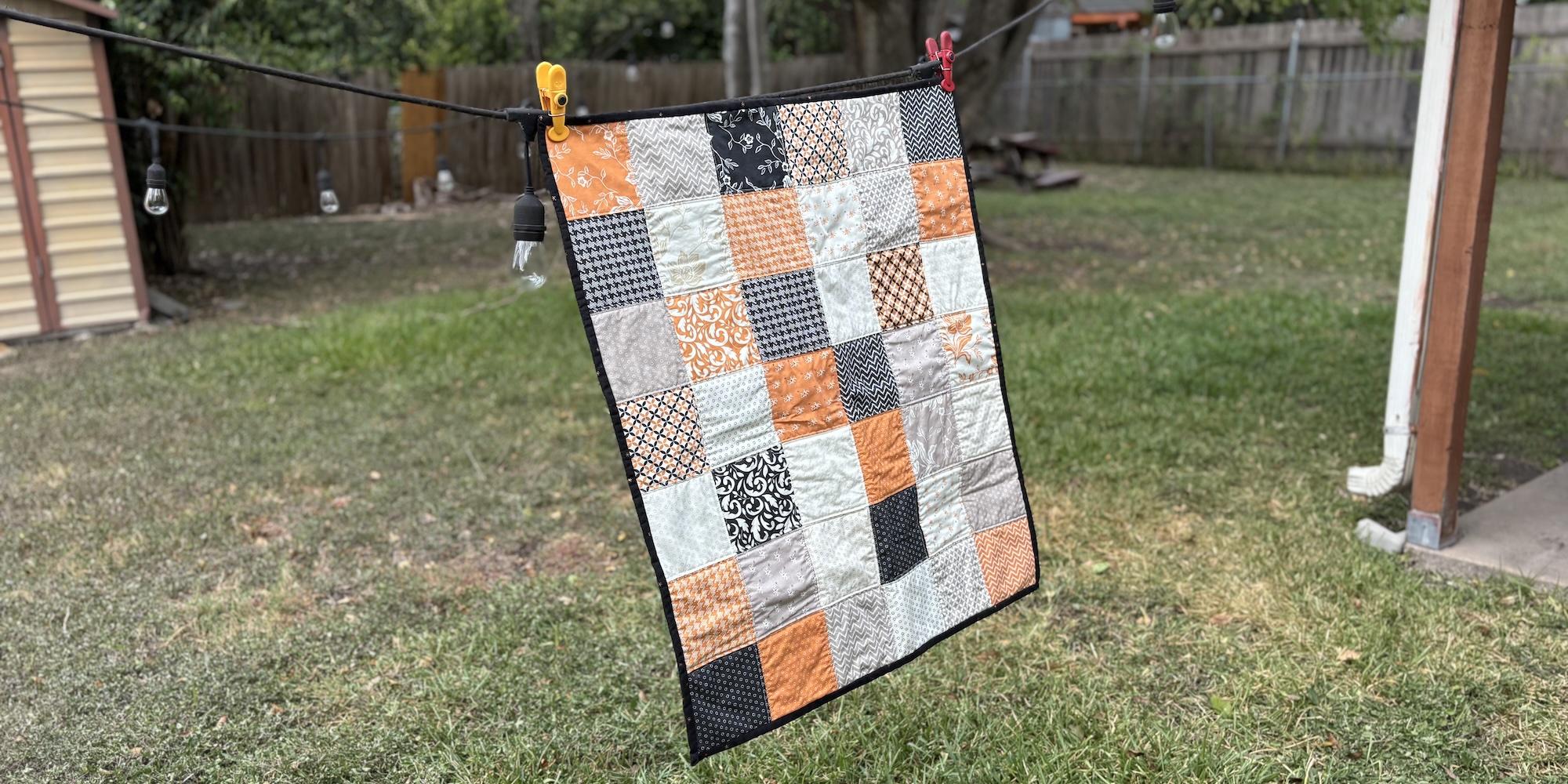 My first quilt, hanging outside with my backyard in the background. It's orange, black and white squares, with a black binding, and a black and white backing.