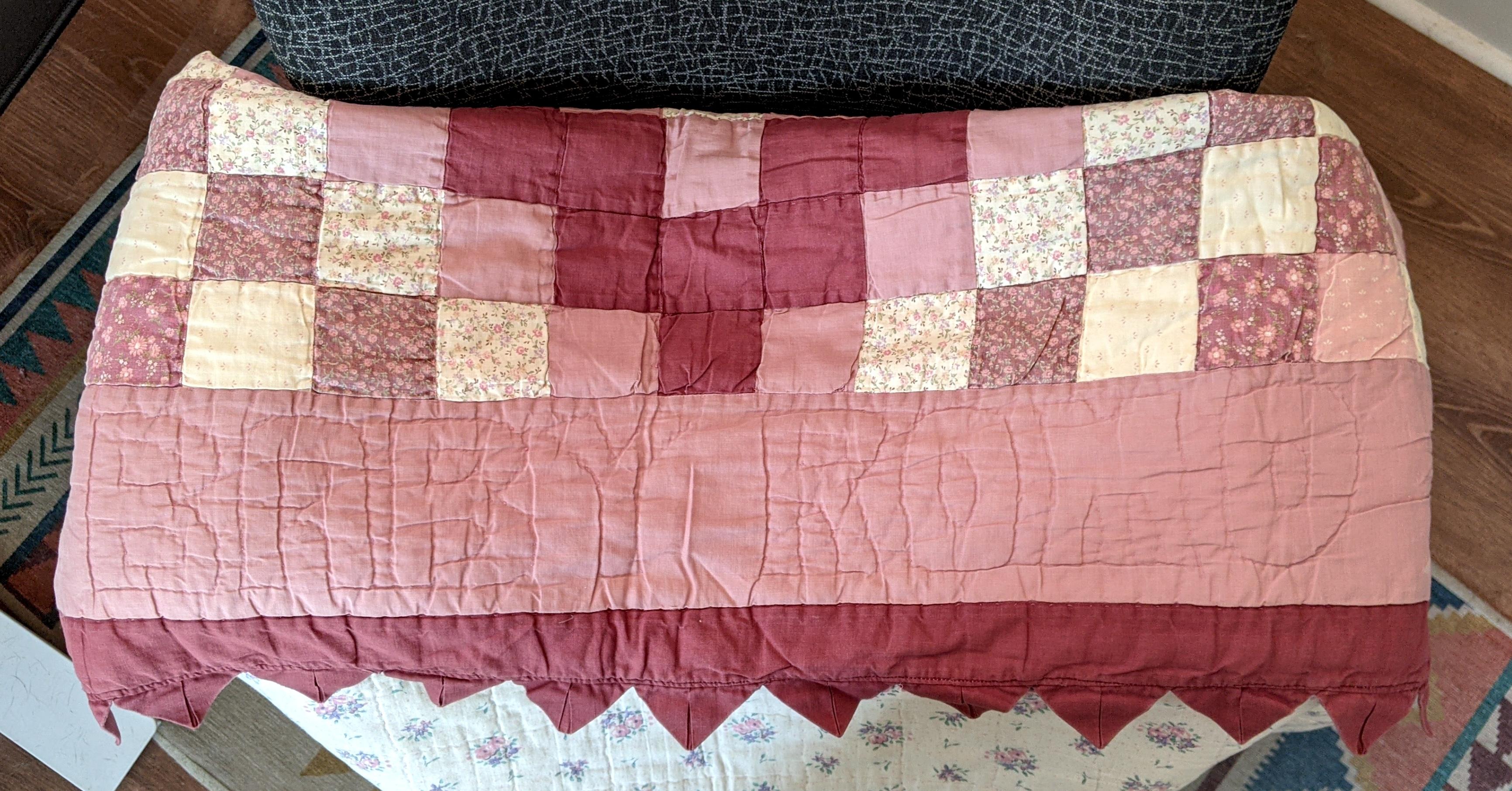 A folded baby quilt with pink and purple floral squares. The words 'Baby Romo' are quilted into one of the sides.