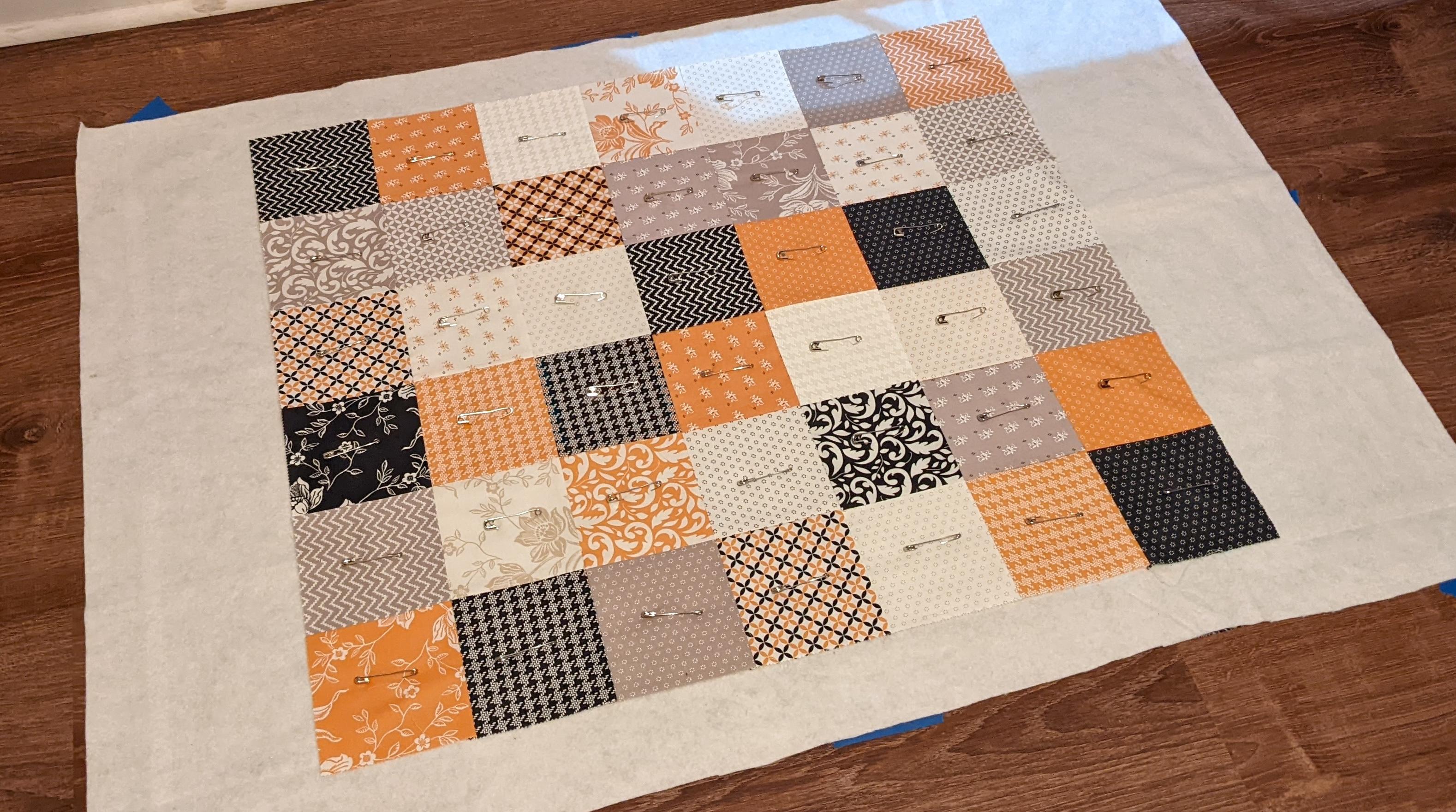The quilt top, batting, and backing fabric laid out on the floor, and pinned together.