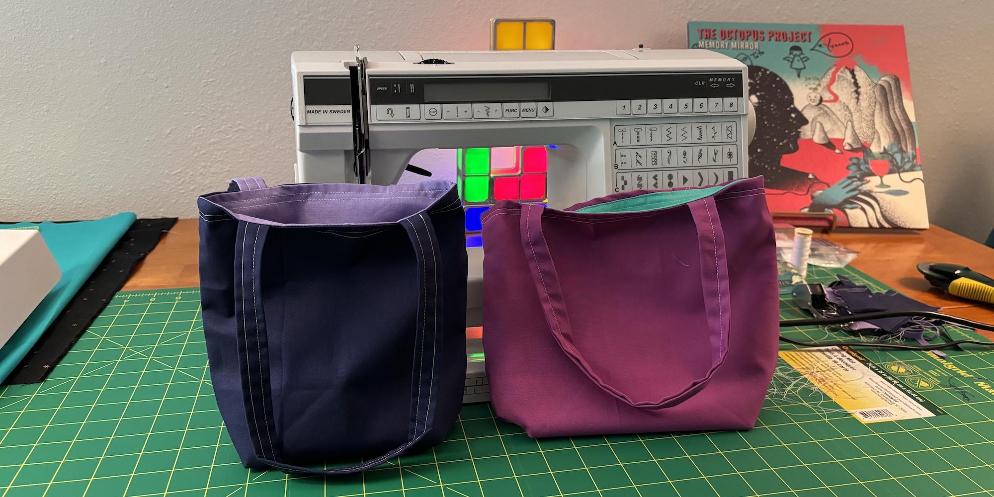 Cover image for this post: Two finished fat quarter totes sitting on my craft table in front of my sewing machine. The left is clearly better made, and the right was clearly made first.